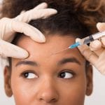 Cosmetic procedures. African-american woman getting botox injection in forehead